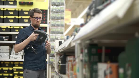 Man is Regarding a Jigsaw in a Hypermarket of Building Tools