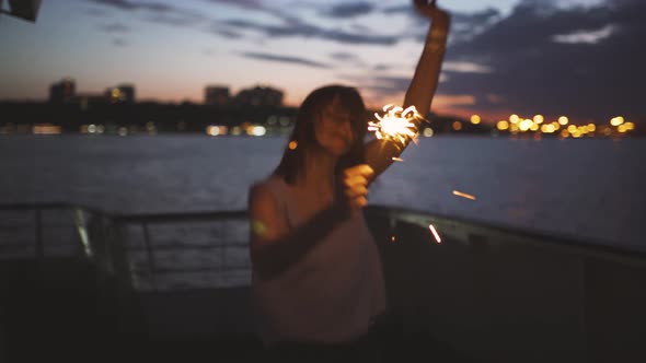 Beautiful Young Woman Dances on the Deck of a Ship with Bengal Lights at Night