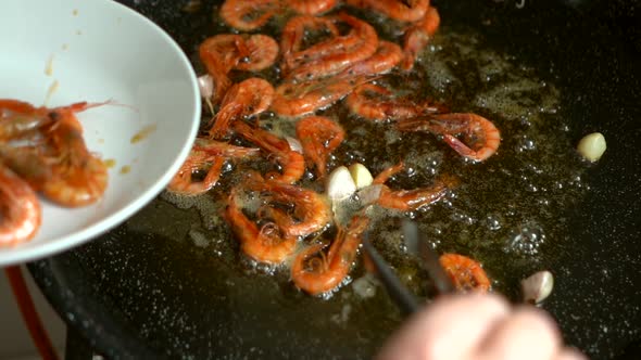 cook removing fried prawns from the heat and putting them on a plate during the preparation of fideu