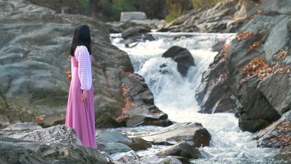 Young pretty woman in long fashionable evening dress standing near small mountain river with fast