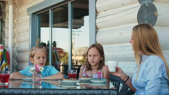 A Young Woman in a Blue Summer Dress with Two Children Spend Their Free Time at a Table