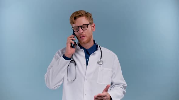 Young Man Doctor Isolated on Blue Background Talking on Smartphone Smiling Positively