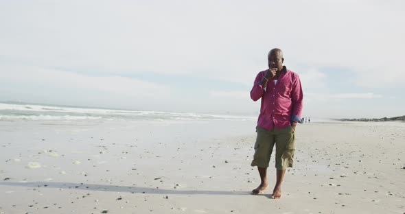 African american senior man walking on a beach rubbing his chin and looking at the sea