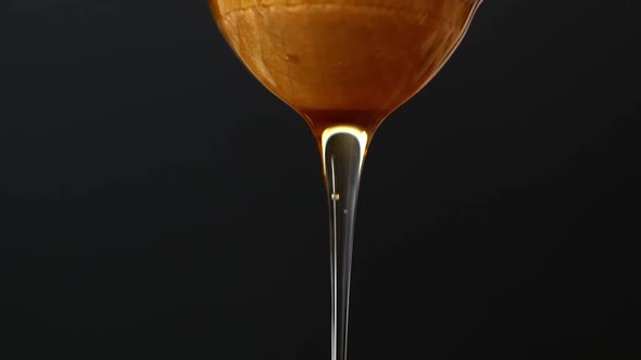 Liquid organic raw honey is poured into a wooden honey spoon.  Macro shot of liquid honey falling