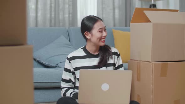 Asian Woman With Cardboard Boxes Comparing The House To Laptop After Moving Into A New House 