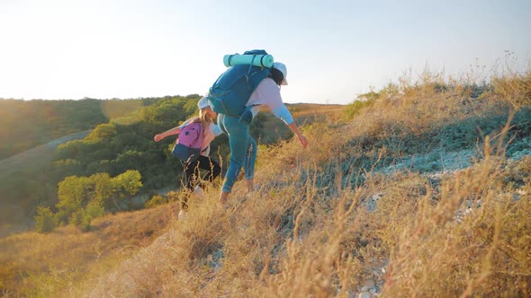 Mother and Daughter with Backpacks Running Through the Meadow at Sunset. Family Tourism Concept.