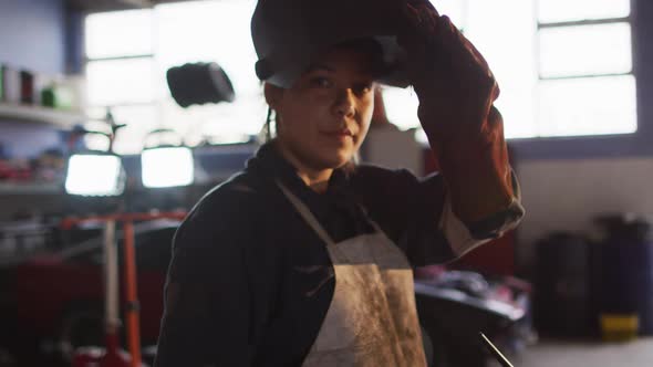 Portrait of female mechanic removing welding helmet at a car service station