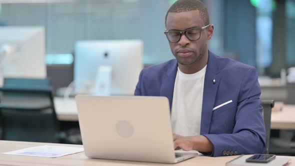Attractive African Businessman Looking at Camera While Using Laptop in Office