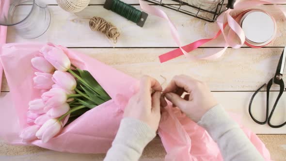 Step by step. Florist wrapping pink tulips in bouquet