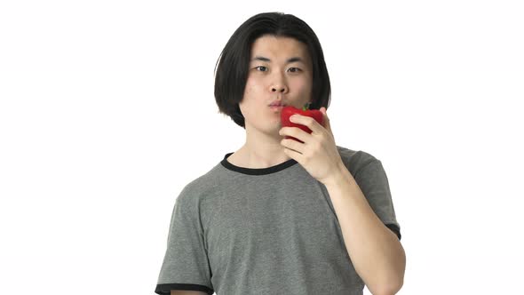 Portrait of Hungry Chinaman with Clean Skin in Casual Gray Tshirt Smiling and Eating Big Red Bell