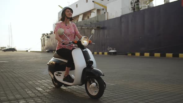 Young Beautiful Girl Riding Near Sea on Scooter at Sunrise