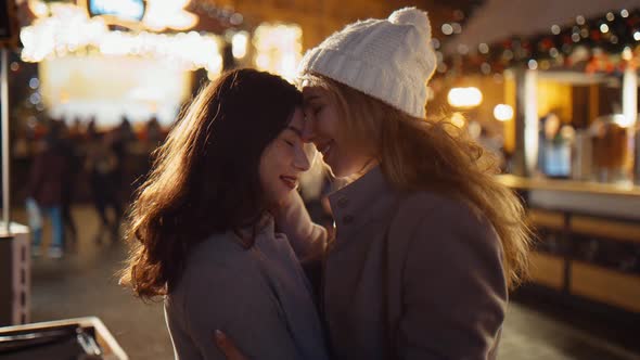 Two Girls Young Lesbian Women Embrace on the Square in the Lights of the Fair on Christmas