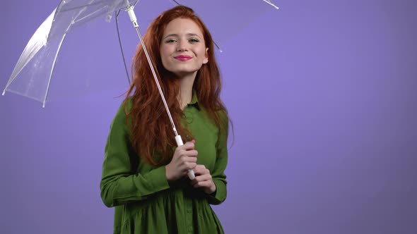 Cute Woman Stands Under Umbrella on Violet Studio Background