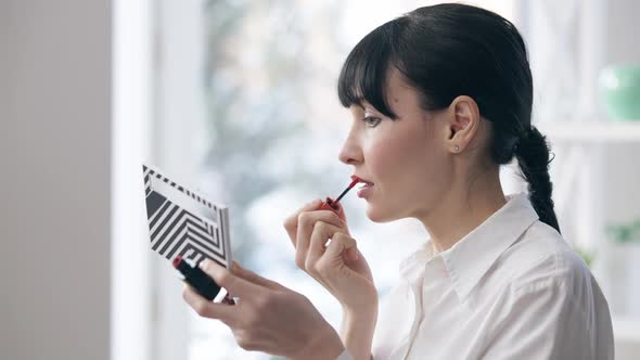 Side View Portrait of Young Slim Confident Businesswoman Applying Lipstick in Office