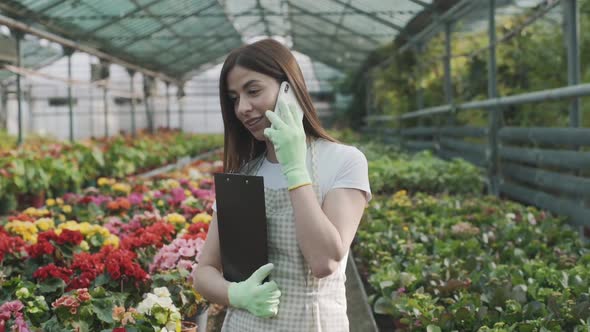 young girl with a folder for notes in her hands in a greenhouse talking on the phone on a background