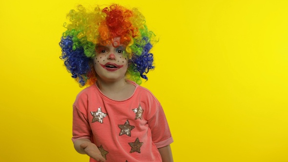 Little Child Girl Clown in Colorful Wig Waving Hands, Having Fun, Smiling. Halloween