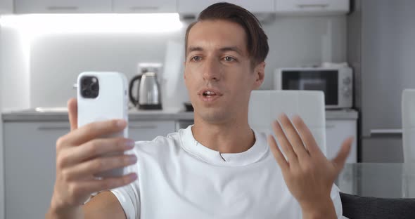 Young Man Holding Smartphone Making Selfie Video Call While Sitting on Couch in Living Room