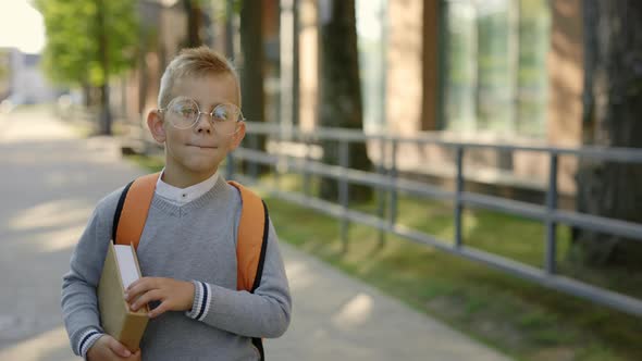 Male Smiled Pupil Wearing Glasses Carrying Backpack Go to School Holding the Book