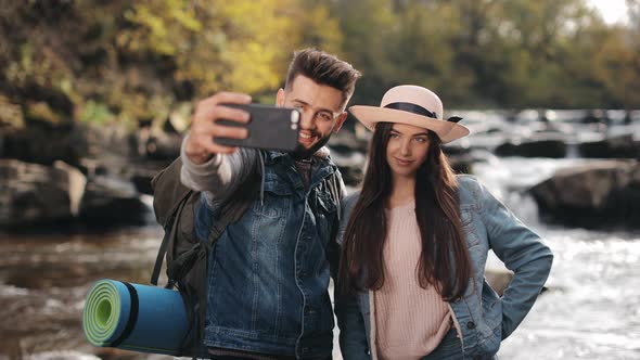 A Young Woman and a Man are Standing on the Shore of a Mountain River