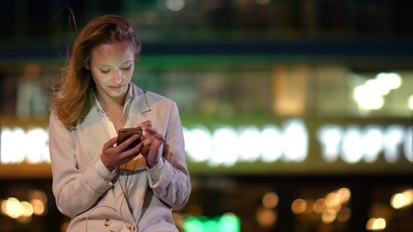 Beautiful woman using her phone late at night when lights