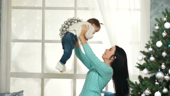 Happy Mom Raises Up His Little Kid Playing Before Christmas Tree