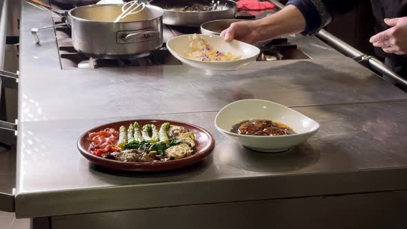 Chef wearing black dress places red fried mullet by a asparagus and roasted pepper salad and a foie