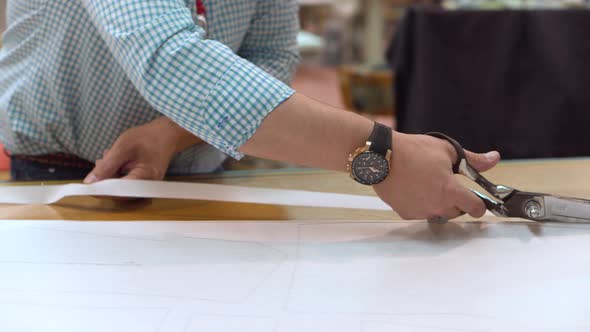 Tailor Cutting Out the Marked Pattern on Fabric with Large Scissors on the Workbench in His Shop