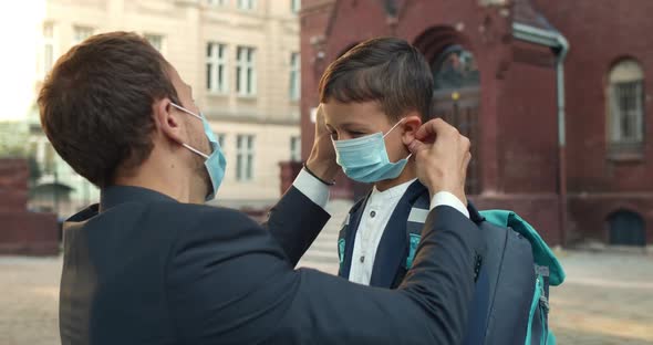 Close Up of Loving Father Wearing Medical Mask on His Son Face While Sending Him To School. Boy with