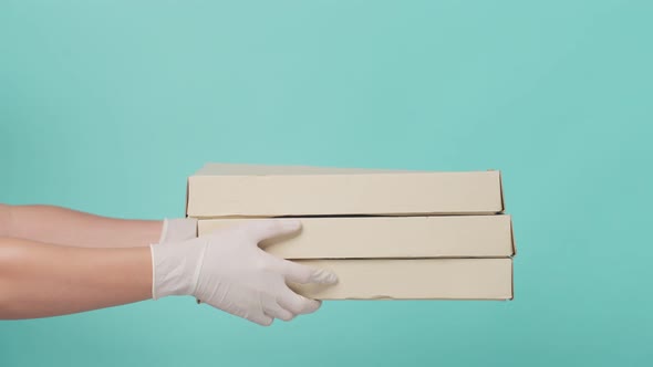 Close up of Asian delivery man wearing hand glove holding pizza box in hands and giving to customer.