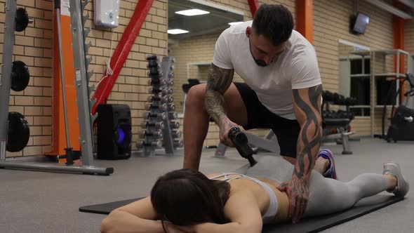 Personal Trainer Using Massage Gun on Body of Sportswoman