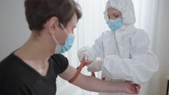 Focused Woman in Protective Suit and Coronavirus Face Mask Tightening Harness on Hand of Man