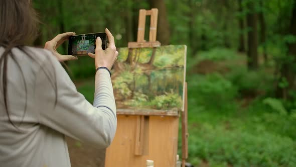 Back View of Brunette Female Paints a Landscape in an Open Air in the Forest and Taking a Photo