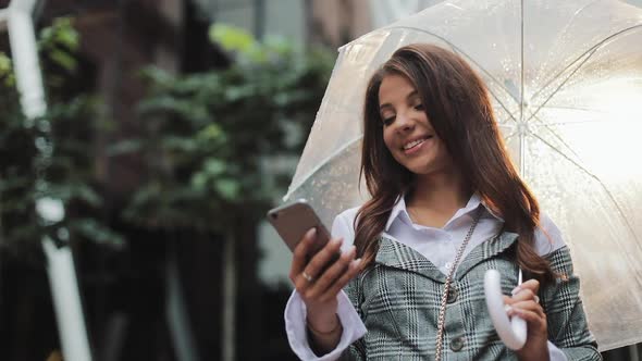 Young Business Woman Using Smartphone on the Street in Rainy Weather Smiling Holding