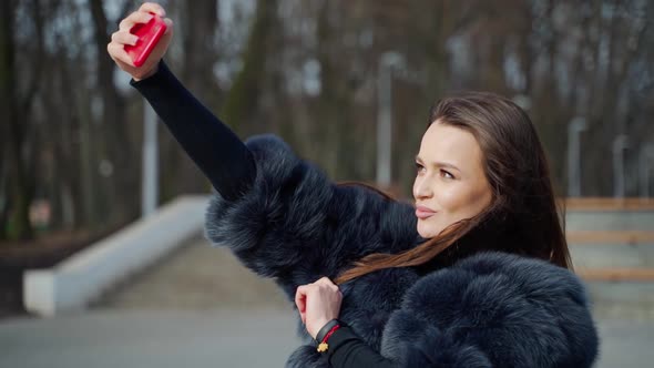 Girl with smartphone in hand. Lifestyle portrait of young positive woman making selfie in park