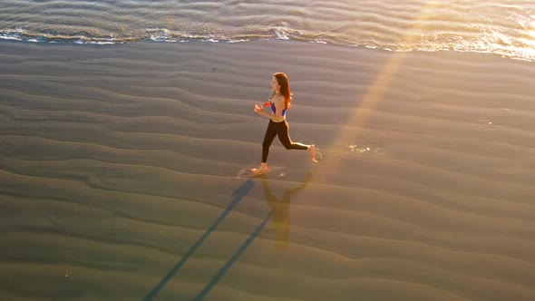 Aerial shot of fit asian woman jogging on the beach at sunset
