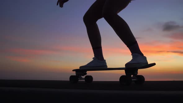 Beautiful Girl Rides a Skateboard on the Road Against the Sunset Sky. Close Up