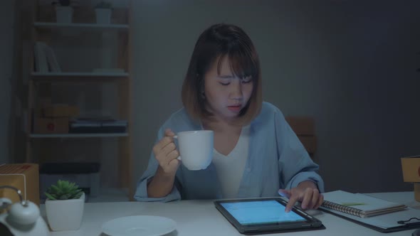 Asian young woman owner of SME online check product on stock and save to tablet and drinking coffee.