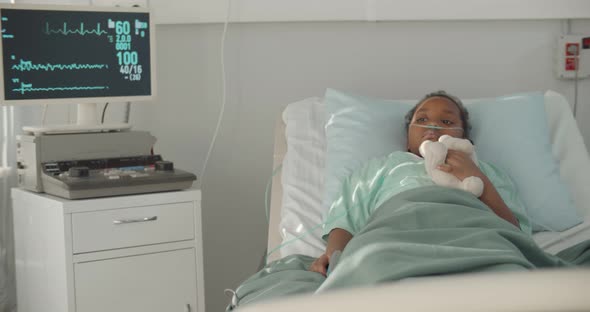 Afroamerican Kid Lying in Hospital Bed with Oxygen Tube and Plush Toy