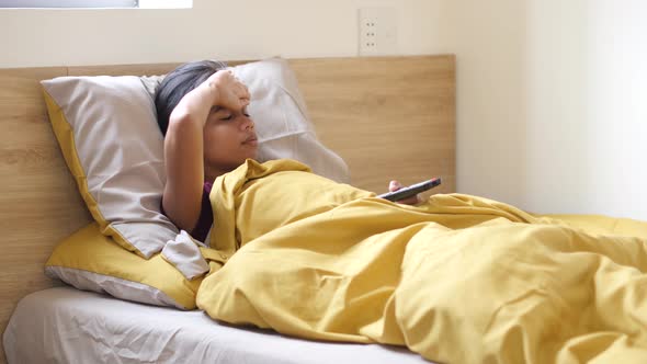 Young Asian Woman Lying in Bed on Home Quarantine Watching News About Covid-19.