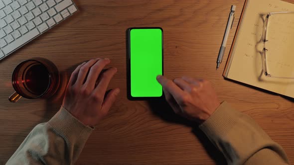 Man Tapping on Green Screen of Mobile While Sitting at Desk
