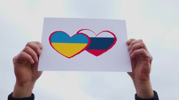 Man Hands Holding of Heart Drawingon and Russian Flag and Ukraine Flag the Cardboard