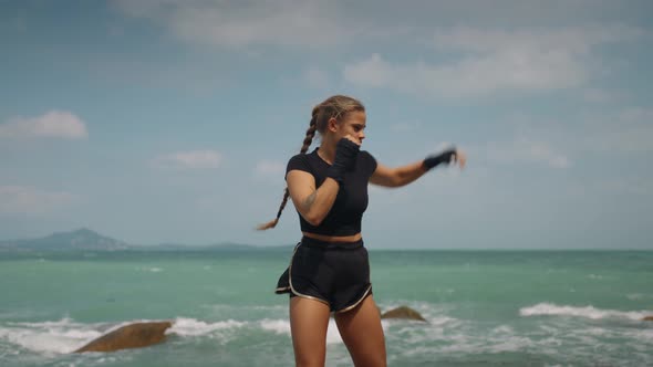 Long Haired Sporty Girl in Black Sportswear Isolated on the Ocean Background Has Boxing Training