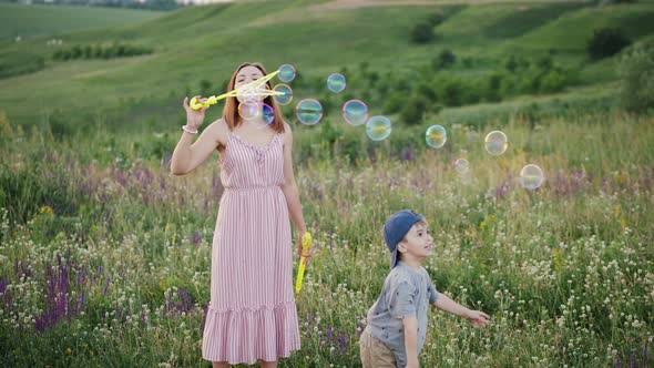 Mom with Little Son Play with Soap Bubbles in Nature