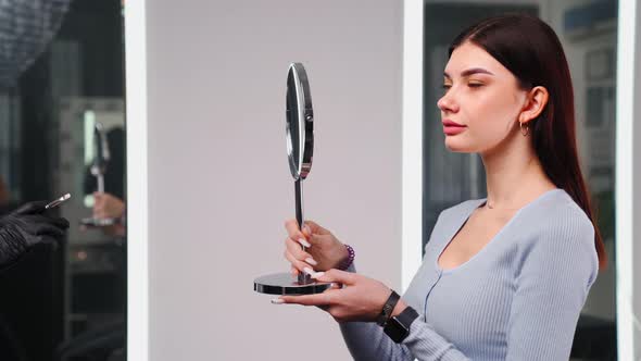 Beautiful Woman with Perfect Skin Face Looks Herself in Mirror in Beauty Salon