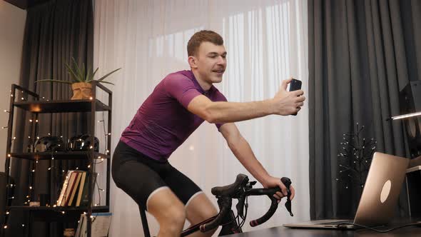 Man is cycling on indoor smart trainer and taking selfies on smartphone