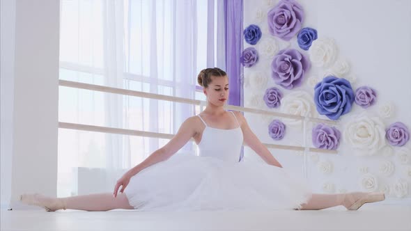 Ballerina in White Tutu and Pointes Stretches Sitting on Twine in Ballet Class