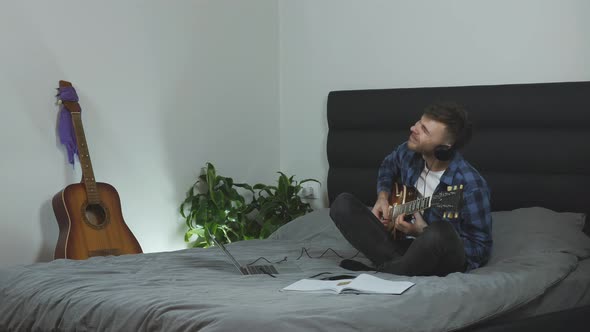 Musician emotionally performs solo on electric guitar on bed in modern living room, Music concept
