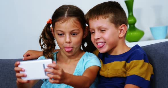 Siblings taking selfie from mobile phone in living room