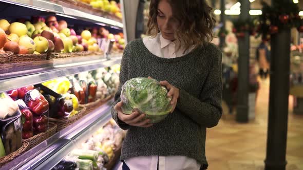 Young Woman in Modern Supermarket Choosing Big Cabbage in Organic Vegetable Department and Put It to