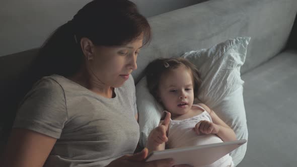 Mom and Little Daughter Are Lying in Bed with a Wake Cartoon on a Tablet. Mother and Baby Make Video